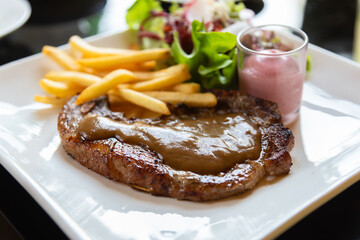 Grilled steak pork meat with fried potatoes, vegetable and gravy in white dish closeup image.