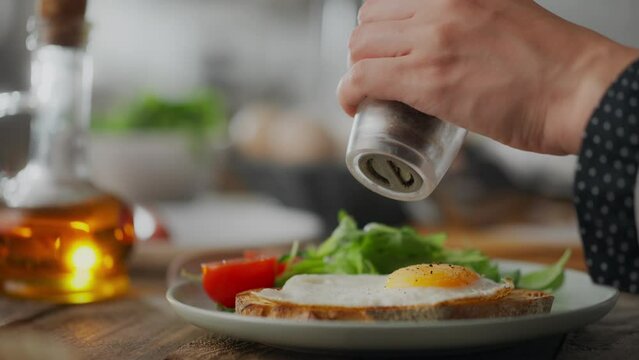 Fry. A middle-aged woman in loungewear fries eggs in a frying pan on a wooden table. Close-up of a healthy eating girl fresh eggs in a frying pan preparing a healthy fresh breakfast
