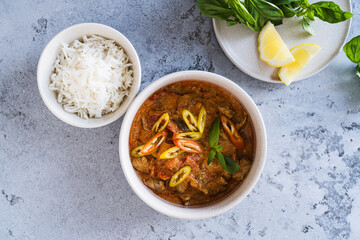 Red curry chicken with white rice in bowl on grey background