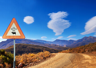 Desert, sign and alien abduction in the mountains with a ufo warning along a dirt road on a blue...