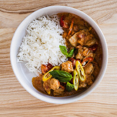 Red curry chicken with white rice in bowl on wooden background
