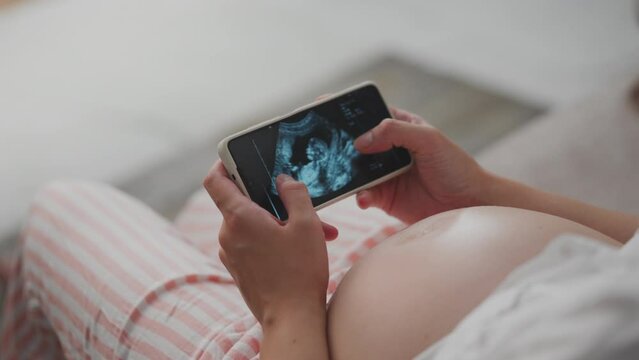 Pending. A girl in light clothes holds a phone in her hands on the screen, a shot of a child’s bridles on a bed at home. Cute girl examines the reins of her child while holding smartphone in her hands