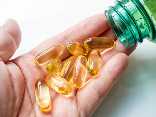 A close-up of cod liver oil capsules, poured from a bottle into the palm of hand. Concept health benefits, nutrition, vitamins, omega 3 and 6, sun, pain relief and vitamin D. 