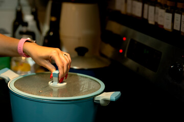   A woman's hand with a beautiful manicure opens the lid of a pan in the kitchen. simple real life photo.
