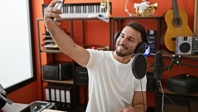 Young arab man musician wearing headphones make selfie by smartphone at music studio