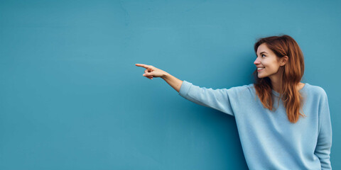 a woman pointing on a plain blue background with copy space, happiness, joy, fashion