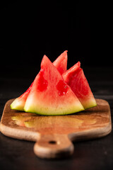 Close-up of watermelon pieces on board, on dark wooden table, black background, vertical, with copy space