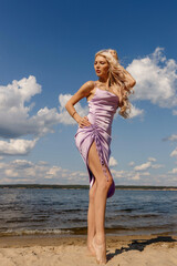 Fototapeta na wymiar a girl in a purple dress on the bank of a river on a sunny day