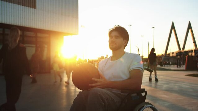A bearded man in a wheelchair holds a basketball at sunset
