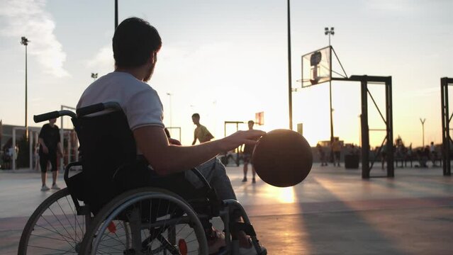 People playing basketball on the background and a man in a wheelchair hitting the basketball on the foreground