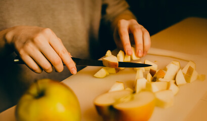 A woman's hands slicing an apple with a knife to prepare a dinner dessert - charlotte. The home cooking and nourishment.