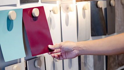 Designer hand picking colorful laminate sheet on material swatch wall display in material library....