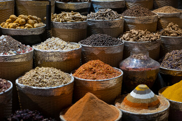 Many baskets and bowls with variety of different traditional colorful aromatic dried spices, flowers, roots and condiments for sale at a local spice market. Selective focus, blurred background.