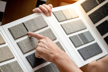 Designer hand pointing on fabric tile carpet samples catalog in material library. Choosing rug...