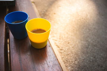 Blue and yellow cups with coffee in morning sunshine. Patriotic ukrainian colours. Two plastic mugs with cappuccino. Portable camping cups. Outdoor dating.  - obrazy, fototapety, plakaty