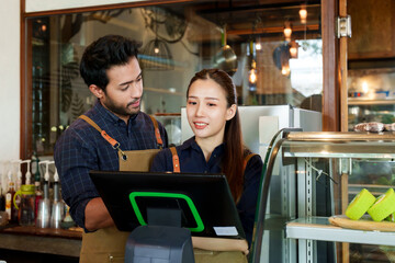 Indian businessman wearing overalls Teaching how to use a cash register with a beautiful wife Seriously standing behind the cashier counter. in coffee shops and bakeries