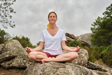 Fototapeta na wymiar A Woman meditating in easy pose while sitting on rock