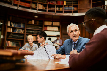 Young African American student getting his paper graded by a professor in a university library