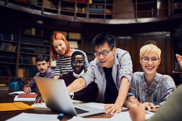 Young and diverse group of students using the laptop and studying in an university library together