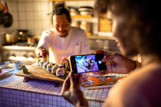 Young African American woman taking pictures of sushi in a sushi restaurant or bar