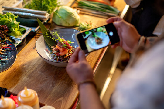 Young and skilled sushi chef taking a picture of the dish he prepared in the kitchen of a sushi restaurant or bar with his smartphone