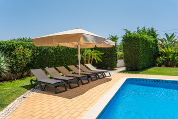 Sunbeds around the pool in the garden with green grass for tourists to relax.