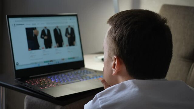 A man chooses clothes in an online store while looking at a laptop screen