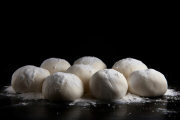 Fototapeta na wymiar Raw dough balls and flour on black background