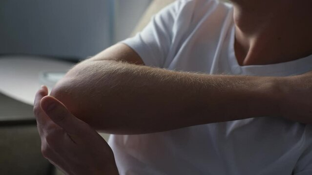 A man kneads his elbow joint with his hand, feeling pain and discomfort, close-up