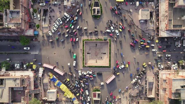 Vertical Top angle aerial drone shot of the crossroads or roundabout with moving vehicles or traffic passing in a busy Indian city market or traditional old bazaar. Urban transportation concept
