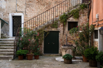 Una tipica corte veneziana con un pozzo, delle piante e una scala che sale al primo piano
