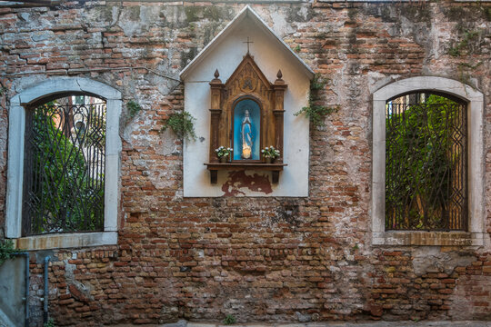 Un tabernacolo dedicato alla Madonna fra due finestre che affacciano su un giardino in una piccola piazza di Venezia