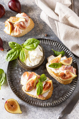 Italian appetizer recipe. Toast or bruschetta with bacon and figs, cream cheese and honey on a gray stone background.