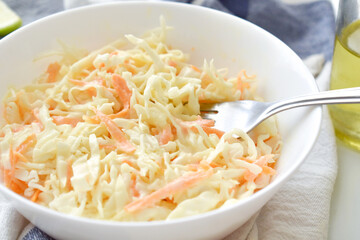 Coleslaw salad with carrot and cabbage in a white bowl.