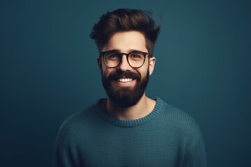 Obraz premium Young handsome man with a beard in a sweater and glasses on a blue background, happy face smiling, looking at the camera. A positive person. Generative AI