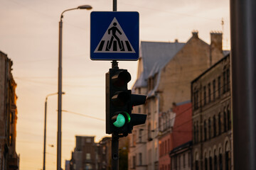 Green traffic light below pedestrian sign showing green light in evening with sunset in the background