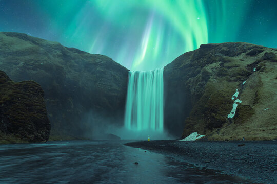 Powerful waterfall flowing through rocky slope under northern lights