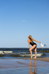 A blonde girl in a black swimsuit sunbathes on the seashore with a white hat in her hands with her eyes closed