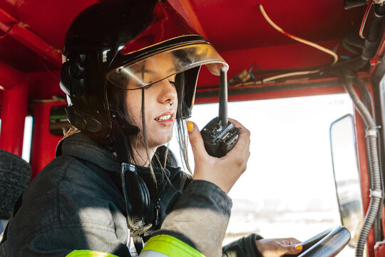 Young female firefighter driving fire truck and talking on radio