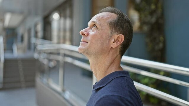 Middle age man, relaxed yet with a serious expression, standing outside looking up to the city's sky from a bustling urban street