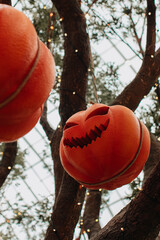 Orange pumpkin with a scary Halloween face hanging on a tree with twinkling garlands. Creative...
