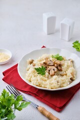 Risotto with mushrooms garnished with parsley in a light plate on a white concrete background. Risotto recipes.