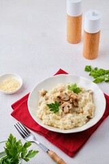 Risotto with mushrooms garnished with parsley in a light plate on a white concrete background. Risotto recipes.