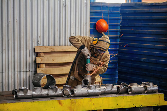 Male worker grinding chamfer of T shape pipe parts in factory