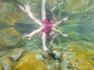 Underwater photo, a small child girl in a pink swimsuit with a snorkel and diving mask is snorkeling at the Rummu quarry.