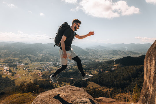 Homem Aventureiro Saltando em Montanhas com Mochila e Vista Panor&acirc;mica Deslumbrante. Salto Confiante na Montanha. Praticante de caminhada ao ar livre saltando em cima de uma pedra. Sequ&ecirc;ncia.