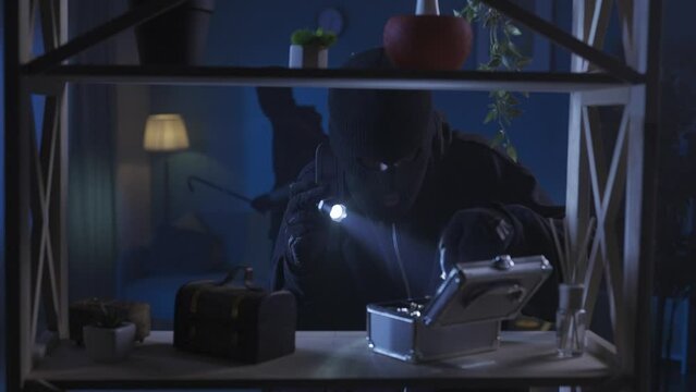 Video capturing two burglars in the room looking for valuables. One of the men is putting jewelry he found on the shelf in his bag, the other is going around on the background. HDR BT2020 HLG Material