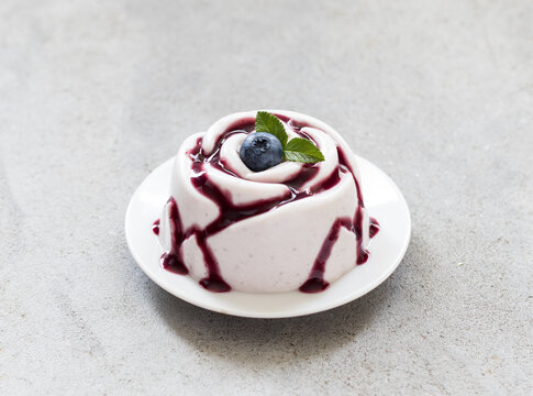 Blueberry cream pudding, Panna Cotta with blueberry sauce, in the shape of a rose, on a plate. Light grey background