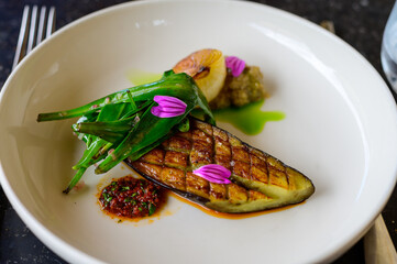 Exquisite vegetarian grilled eggplant dish of modern French haute cuisine prepared with fresh organic ingredients from restaurant own garden and farm and beautifully served