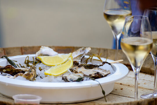 Fresh french Gillardeau oysters molluscs shucked on ice with lemon ready to eat with glasses of champagne sparkling wine close up